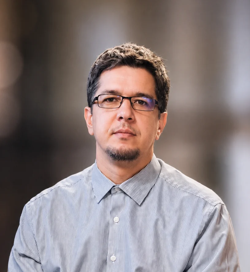 Portrait of Milot S. Mehmeti wearing glasses and a striped shirt